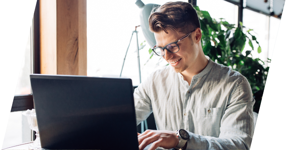 Junger Mann mit Brille und grauem Hemd sitz vor Notebook